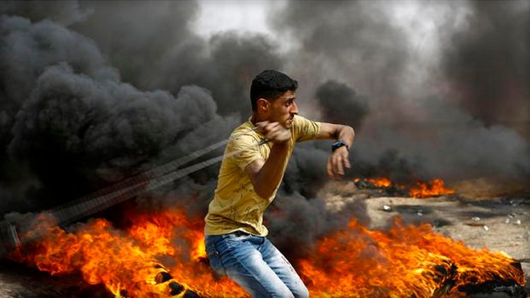 A Palestinian slings a shot by burning tires during clashes with Israeli forces across the border, following a demonstration calling for the right to return — meaning Palestinian refugees being allowed to go back to the land they fled or were expelled from during the 1948 war surrounding Israel's creation — near the border with Israel, east of Gaza City, in the southern Gaza Strip, on April 20, 2018.  MOHAMMED ABED / AFP/GETTY IMAGES