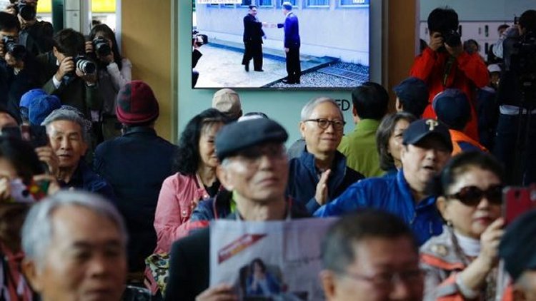 In this April 27, 2018 photo, People watch a TV screen showing the live broadcast of South Korean President Moon Jae-in, top right, meets with North Korean leader Kim Jong Un at the border village of Panmunjom during a news program at the Seoul Railway Station in Seoul, South Korea  (AP Photo/Ahn Young-joon)