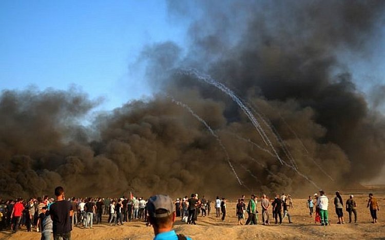 Palestinian protesters gather in the smoke billowing from burning tyres as Israeli forces launch tear gas canisters at the Israel-Gaza border, east of Gaza city, on October 12, 2018. (Photo by SAID KHATIB / AFP)